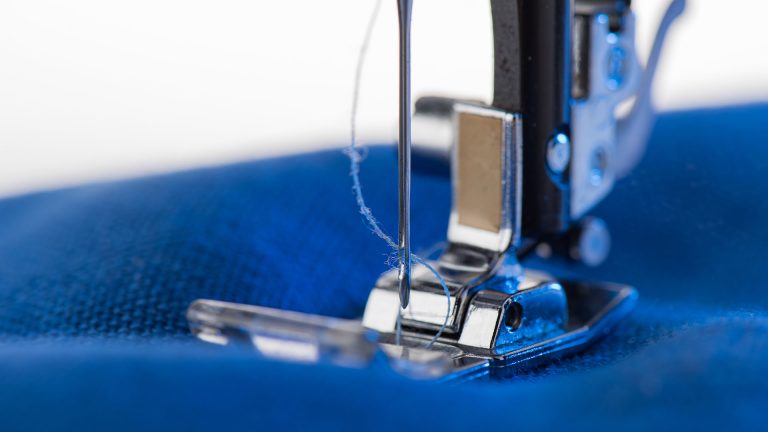 Close-up view of working sewing machine sewing blue fabric
