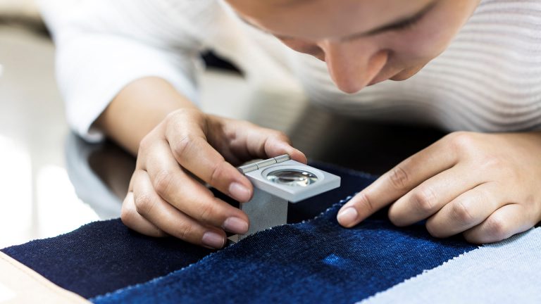 Young woman examining fabric quality with magnifier