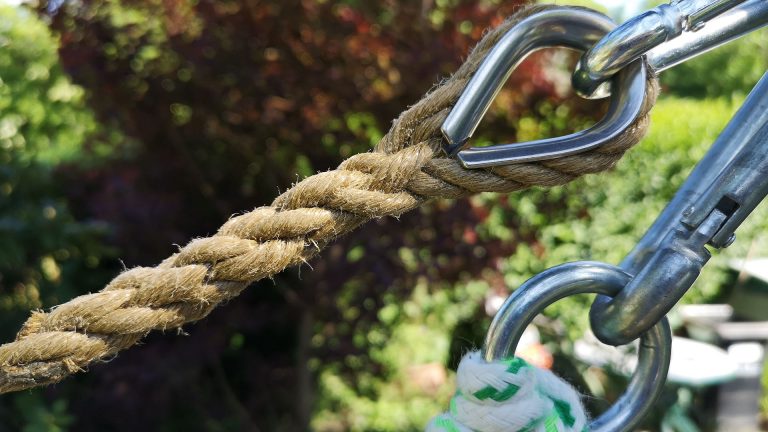 Closeup view of a traditional rope with splice and thimble and a modern rope with knot and metal ring. Trees in the blurred background